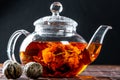 Tea in a glass teapot with a blooming large flower. Teapot with exotic green tea-balls blooms flower. Tea ceremony on a dark Royalty Free Stock Photo