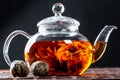 Tea in a glass teapot with a blooming large flower. Teapot with exotic green tea-balls blooms flower. Tea ceremony on a dark Royalty Free Stock Photo