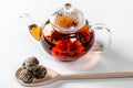 Tea in a glass teapot with a blooming large flower. Teapot with exotic green tea on a white background with dried balls-buds for