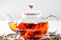 Tea in a glass teapot with a blooming large flower. Teapot with exotic green tea on a white background with scattered dried tea Royalty Free Stock Photo