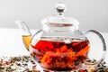 Tea in a glass teapot with a blooming large flower. Teapot with exotic green tea on a white background with scattered dried tea Royalty Free Stock Photo