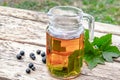 Tea in a glass teapot with green leaves of black currant on a wooden table against the background of green grass Royalty Free Stock Photo