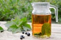 Tea in a glass teapot with green leaves of black currant on a wooden table against the background of green grass Royalty Free Stock Photo