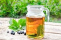 Tea in a glass teapot with green leaves of black currant on a wooden table against the background of green grass Royalty Free Stock Photo