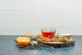 Tea in a mug with herbs, orange, spices, waffle, thread, wooden board, strainer side view on white and stucco background