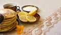 Tea in a painted Cup, on a saucer sliced lemon, pancakes, sour cream and a wooden spoon for overlaying. tea party in rustic style Royalty Free Stock Photo