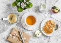 Tea, pancake, apple sauce, homemade gift in kraft paper, flower violet on a light background. Romantic breakfast table.