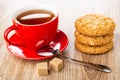 Tea in cup on saucer, spoon, stack of oat cookies with peanut, sugar on wooden table