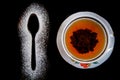 Tea spoon silhouette made with flour on black background and cup of black tea with plate