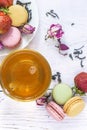 Tea time with french macaroons: cup of tea, traditional french macaroons, dry tea, rose buds on the white paint wooden background Royalty Free Stock Photo