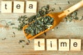 Tea time inscription, Chinese, Japanese green dried tea leaves at bamboo scoop on wooden background