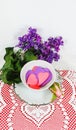 Tea time - Silver trimmed saucer and teacup filled with cutout paper hearts witting on lace doily with heart motif with purple flo