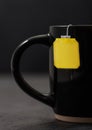 Teabag with yellow blank tag of black tea in black ceramic cup on dark board