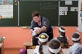 Teacher adjusts the bow on the schoolgirl, who sits at her desk, against the background of the school board in the school class.