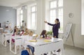 School children sitting at desks and raising their hands up to answer teacher's questions Royalty Free Stock Photo