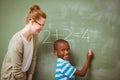 Teacher assisting boy to write on blackboard in classroom Royalty Free Stock Photo
