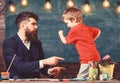 Teacher with beard, father and little son having fun in classroom, chalkboard on background. Fatherhood concept. Child