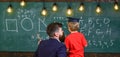 Teacher with beard, father teaches little son in classroom, chalkboard on background. Boy, child in graduate cap Royalty Free Stock Photo