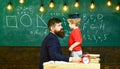 Teacher with beard, father teaches little son in classroom, chalkboard on background. Boy, child in graduate cap play Royalty Free Stock Photo
