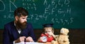 Teacher with beard, father teaches little son in classroom, chalkboard on background. Individual lesson concept. Boy Royalty Free Stock Photo