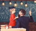 Teacher with beard, father teaches little son in classroom, chalkboard on background. Instructive conversation concept