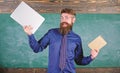 Teacher bearded hipster holds book and laptop. What would you prefer. Teacher choosing modern teaching approach. Paper