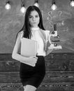 Teacher of biology holds book and microscope. Biology concept. Lady in formal wear on calm face in classroom. Lady Royalty Free Stock Photo