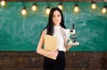 Teacher of biology holds book and microscope. Biology concept. Lady scientist holds book and microscope, chalkboard on
