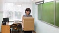 A teacher with a box of personal belongings leaves the school classroom, the concept of dismissal