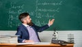 Teacher charismatic hipster sit at table classroom chalkboard background. Educational conversation. Talking to students