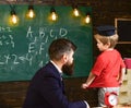 Teacher and child talking in the classroom. Little schoolboy in Oxford cap answering the question in front of the green Royalty Free Stock Photo