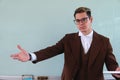 Teacher dressed in brown jacket at a blackboard with open hands. Elegant man giving a class in university. A teacher in Royalty Free Stock Photo