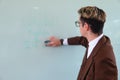 Teacher erasing the blackboard. Caucasian teacher, blond and smartly dressed in a brown suit and wearing glasses.