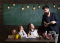 Teacher and girls pupils in classroom, chalkboard on background. Man with beard teaches schoolgirls, reading book