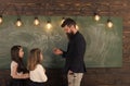 Teacher and girls pupils in classroom near chalkboard. Curious concentrated children listening teacher with attention