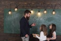 Teacher and girls pupils in classroom near chalkboard. Man with beard in formal suit teaches schoolgirls physics