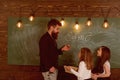 Teacher and girls pupils in classroom near chalkboard. Man with beard in formal suit teaches schoolgirls physics