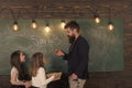 Teacher and girls pupils in classroom near chalkboard. Man with beard in formal suit teaches schoolgirls physics