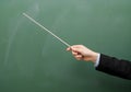 Teacher hand holding pointer stick in front of green chalkboard symbolizing education instruction and knowledge transfer AI Royalty Free Stock Photo
