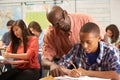 Teacher Helping Male Pupil Studying At Desk In Classroom