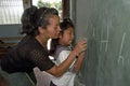 Teacher helping pupil writing on chalkboard