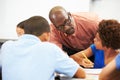 Teacher Helping Pupils Studying At Desks In Classroom Royalty Free Stock Photo