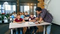 Teacher helping school kids with test tasks in classroom at primary school.