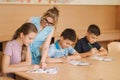 Teacher helping school kids writing test in classroom. education, elementary school, learning and people concept