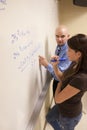 Teacher helping student with a math problem on a whiteboard.