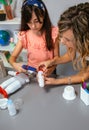 Teacher helping to girl make recycled toy robot with hot melt glue gun