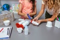 Teacher helping to girl make recycled toy robot with hot melt glue gun