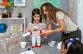 Teacher helping to girl make recycled toy robot with plastic packages