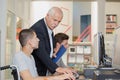 Teacher helping young men using computers one in wheelchair Royalty Free Stock Photo
