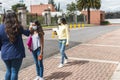 A teacher with her back turned to measure the temperature with an infrared thermometer of a teenage Latina student while another